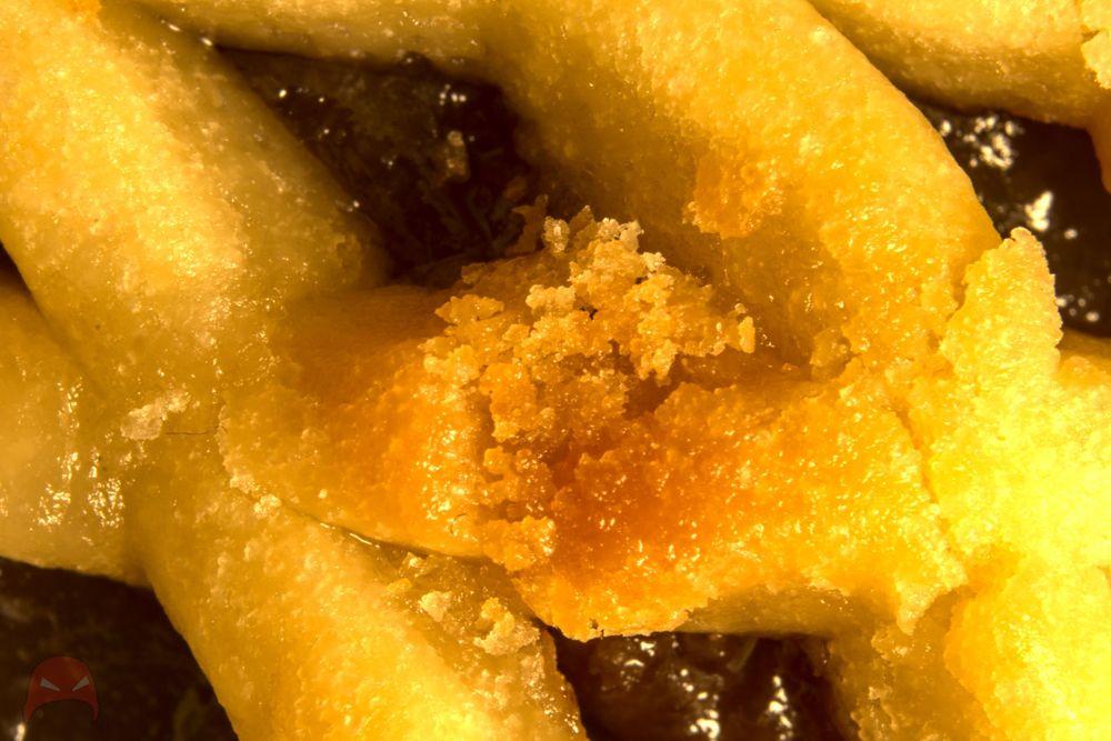 A close up of the lattice work pastry on a fruit mince pie. In the middle of the image is a broken piece of pastry with crumbs falling into the fruit mince mixture