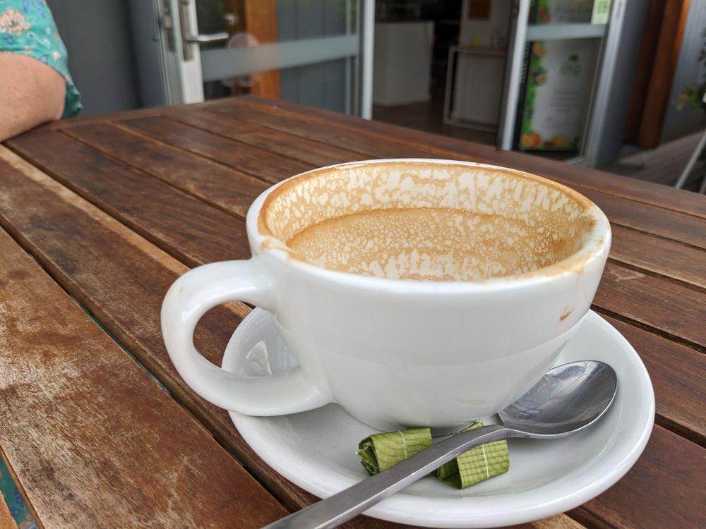 An empty cup of coffee sits on a wooden table. On the saucer underneath is a spoon and two neatly folded empty packets of sugar