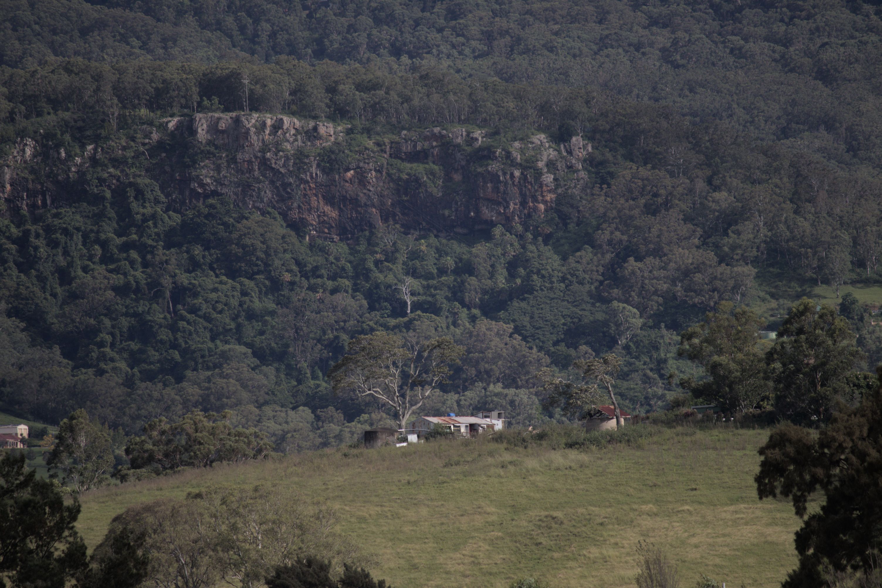 The image presents a tranquil view of a mountainous landscape, with lush greenery covering the slopes and a small community nestled at its base.