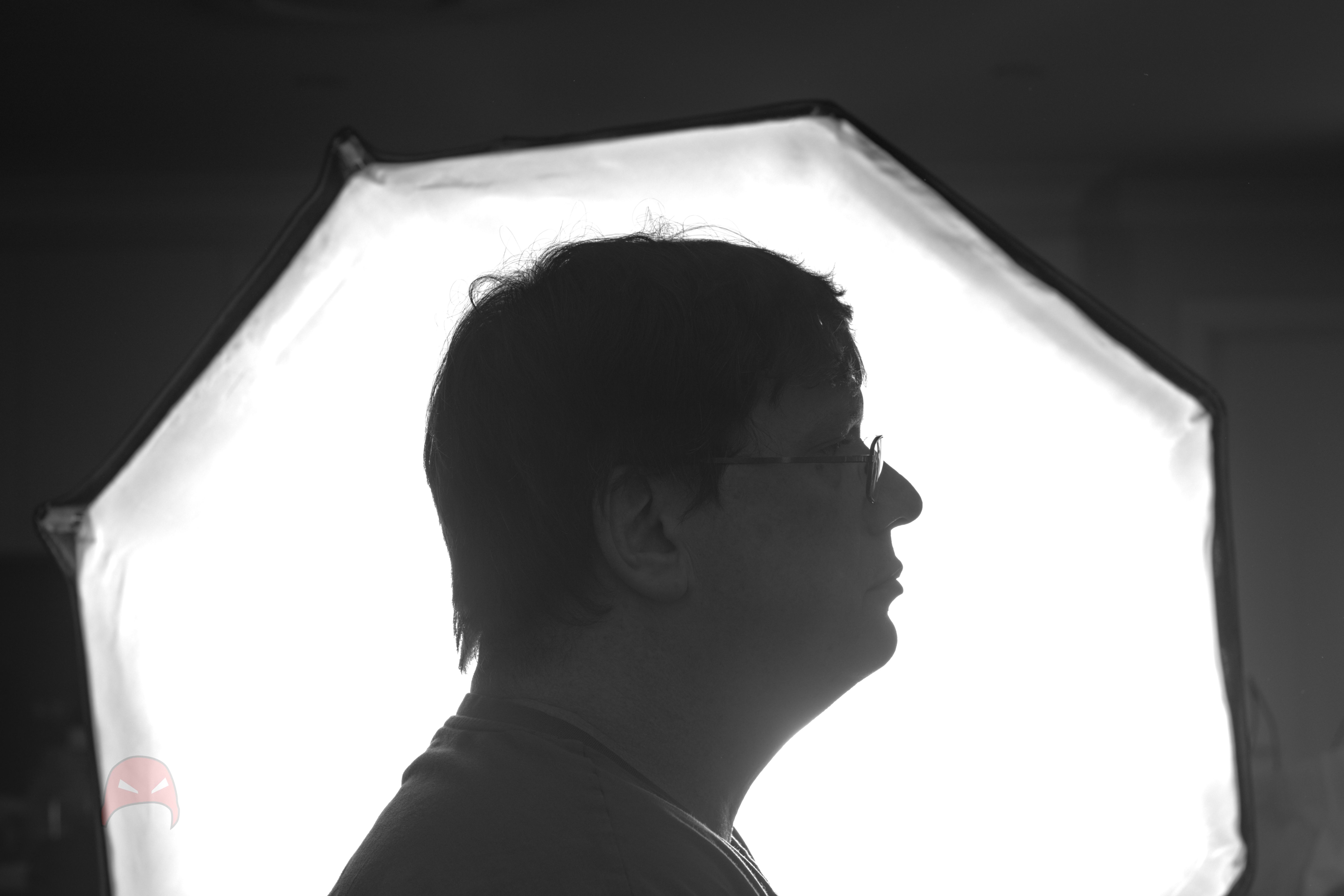 A black and white photo of a man sitting in front of an octagonal light source. The light is on and the man is in silhouette